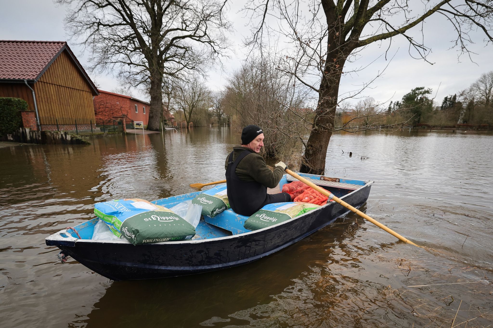 Ein Anwohner bringt mit einem kleinen Ruderboot Futter für seine Tiere über eine überschwemmte Straße in Hagen-Grinden zu seinem Hof. Foto: Christian Charisius/dpa